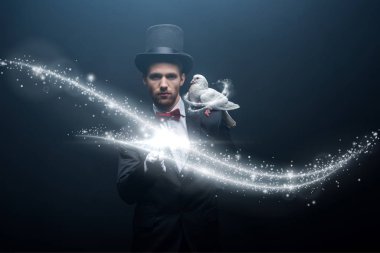 dove sitting on shoulder of young magician in hat with wand in dark room with smoke and glowing illustration clipart