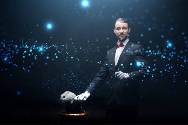 Takım elbiseli mutlu sihirbaz sihirli değnek ve şapkalı beyaz tavşan, dumanlı karanlık oda ve parlayan illüstrasyonla numara yapıyor.
