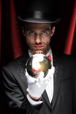 Profesyonel sihirbaz kırmızı perdeli sirkte parlayan resimli sihirli topu tutuyor.