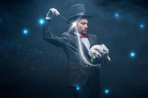 スーツ姿の感情の魔術師と杖と白いウサギのトリックを示す帽子煙と輝くイラストの暗い部屋 — ストック写真