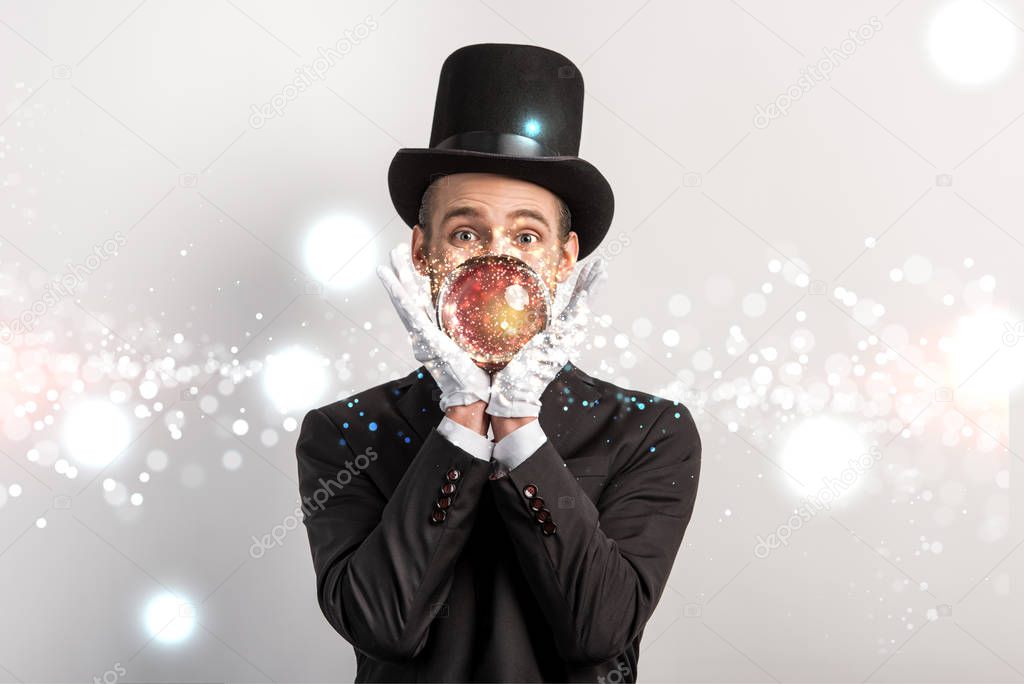 professional magician holding magic ball isolated on grey with glowing illustration