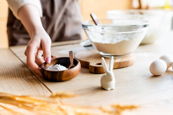 обрезанный вид женщины, держащей миску с выпечкой порошок рядом с декоративным пасхального кролика и яйца
 