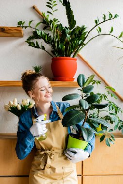 happy woman holding spray bottle and green plant 