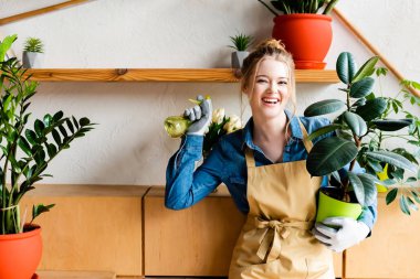 happy young woman holding spray bottle and green plant 