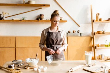 attractive woman looking at bowl near ingredients and figurines with decorative bunnies 
