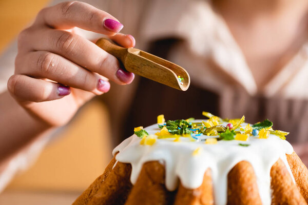 cropped view of woman holding wooden spoon with sprinkles near tasty easter cake 