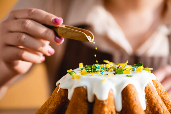 cropped view of girl holding wooden spoon with sprinkles near tasty easter cake 