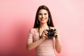 glücklicher Fotograf lächelt, während er die Digitalkamera auf rosa Hintergrund hält