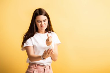 Sinirli kız, telefon görüşmesinde orta parmağını gösteriyor. Sarıda izole edilmiş.