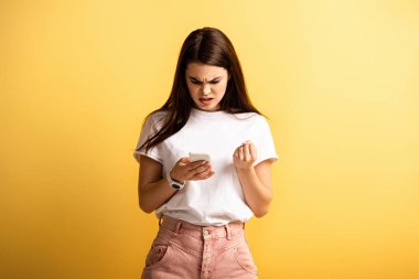 Sinirli kız, sarı arka planda akıllı telefonla konuşurken yumruğunu sıktı.