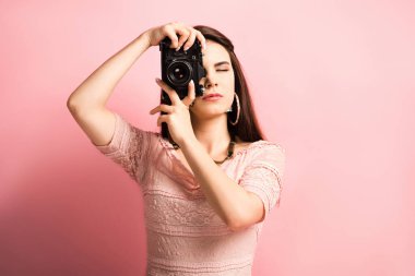 Güzel fotoğrafçı pembe arka planda dijital kamerada fotoğraf çekiyor.