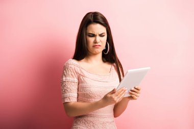 Pembe arka planda dijital tablete bakarken suratını buruşturan hoşnutsuz kız