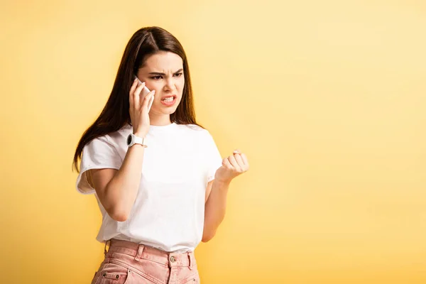 Сердитая Девушка Держит Сжатый Кулак Разговаривая Смартфоне Изолированном Желтый — стоковое фото