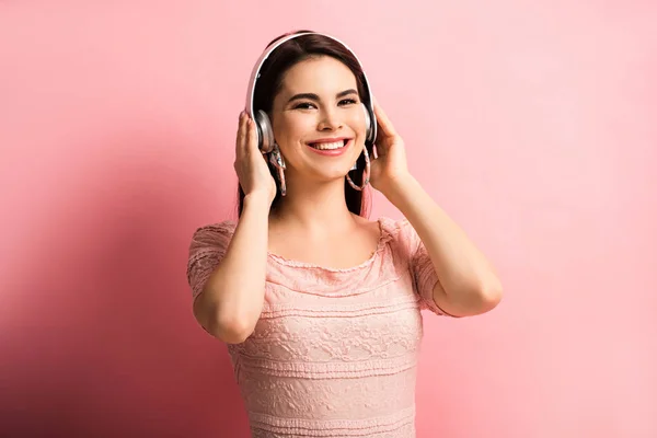 Alegre Chica Tocando Auriculares Inalámbricos Mientras Mira Cámara Fondo Rosa —  Fotos de Stock