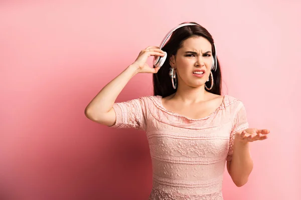 Displeased Girl Touching Wireless Headphones While Standing Open Arm Pink — Stock Photo, Image