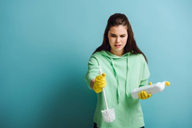 Elinde tuvalet temizleyicisi ve lavabo pompası tutan hoşnutsuz ev kadını.