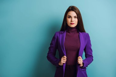 Çekici, kendine güvenen bir kız mavi arka planda dururken kameraya bakıyor.