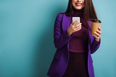 Mavi arka planda kahve içerken akıllı telefondan konuşan gülümseyen bir kızın görüntüsü.