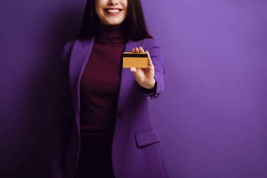 cropped view of smiling woman showing credit card on purple background clipart