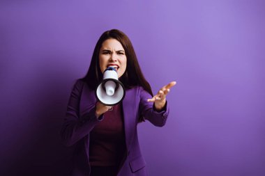 irritated young woman screaming in megaphone while showing indignation gesture on purple background clipart