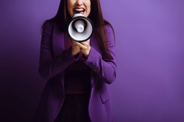 cropped view of excited woman screaming in megaphone on purple background clipart