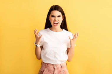 irritated girl gesturing and shouting while showing indignation gesture isolated on yellow clipart