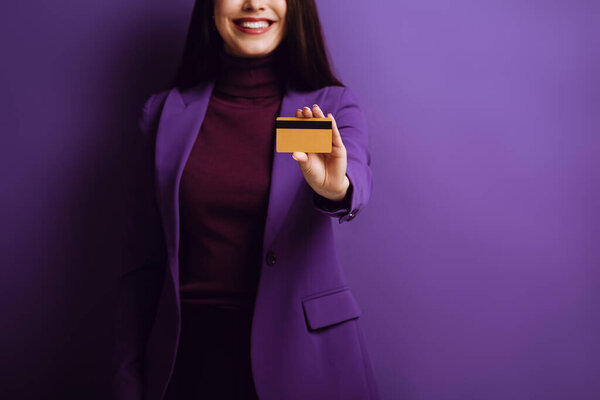 cropped view of smiling woman showing credit card on purple background