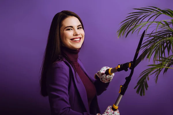 Uśmiechnięta Młoda Kobieta Kroi Roślinę Nożyczkami Ogrodowymi Fioletowym Tle — Zdjęcie stockowe