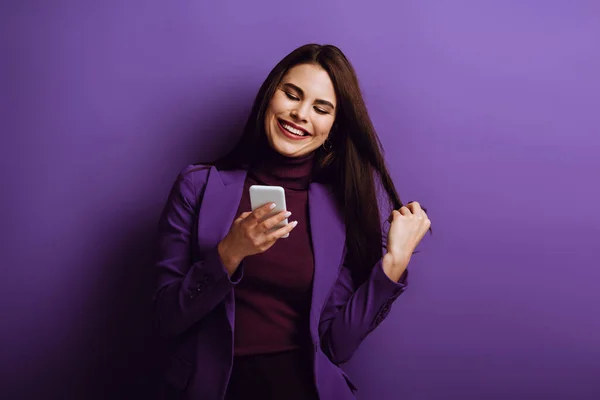 Happy Young Girl Touching Hair Smiling While Chatting Smartphone Purple — Stock Photo, Image