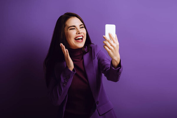happy girl waving hand while having video call on purple background