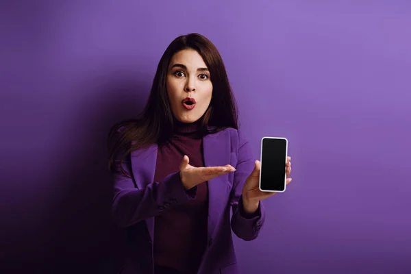 Wstrząśnięta Dziewczyna Wskazując Ręką Smartfona Pustym Ekranem Fioletowym Tle — Zdjęcie stockowe