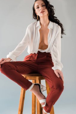 Tişörtlü ve pantolonlu çekici ve seksi bir kadın gri taburede yalnız başına oturuyor.