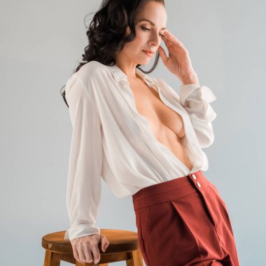 Tişörtlü ve pantolonlu çekici ve seksi bir kadın. Gri tabureye yakın duruyor. 