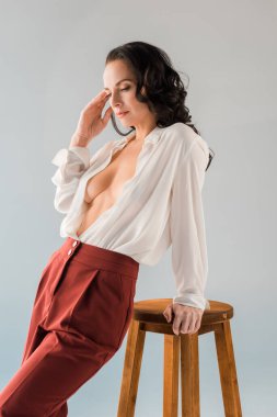 Tişörtlü ve pantolonlu çekici ve seksi bir kadın. Gri tabureye yakın duruyor. 