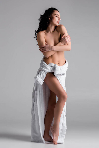 sexy and naked woman in bathrobe obscuring breast on grey background 