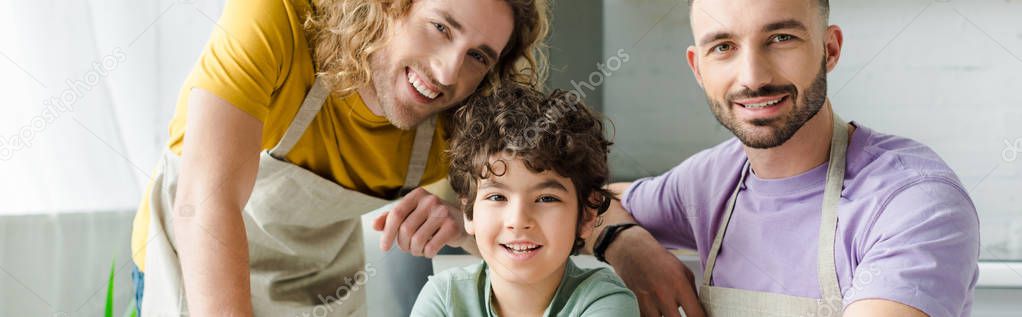 panoramic shot of mixed race kid near happy homosexual parents 
