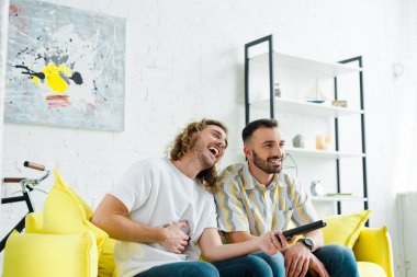 Mutlu homoseksüel erkekler oturma odasında televizyon izlerken gülerler. 