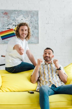 Homoseksüel erkekler oturma odasındaki lgbt bayrağının yanında gülümsüyor. 