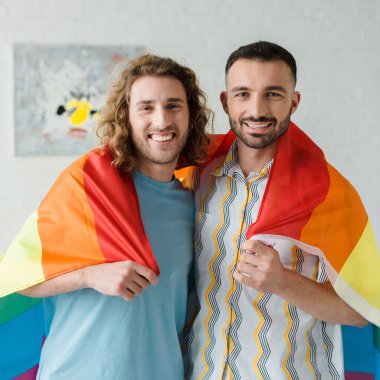 cheerful homosexual men holding lgbt flag and looking at camera  clipart