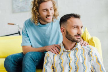 Mutlu homoseksüel erkekler oturma odasında otururken gözlerini kaçırıyorlar.  