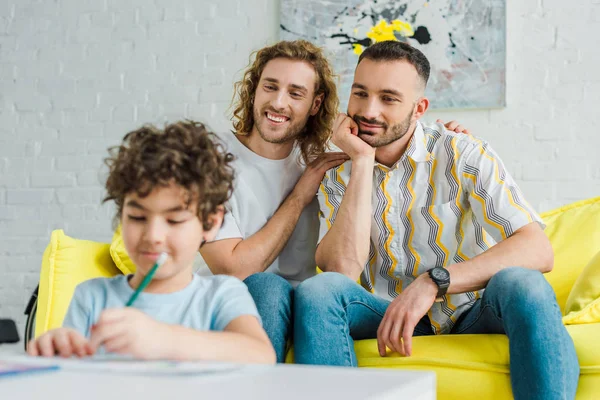 家庭で描かれた複雑な人種の息子を見て幸せな同性愛者の両親の選択的焦点 — ストック写真
