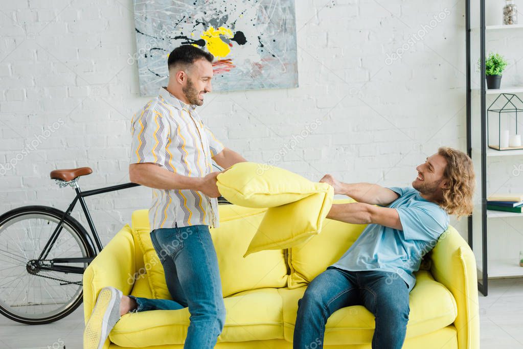 Side view of happy homosexual men pillow fighting in living room