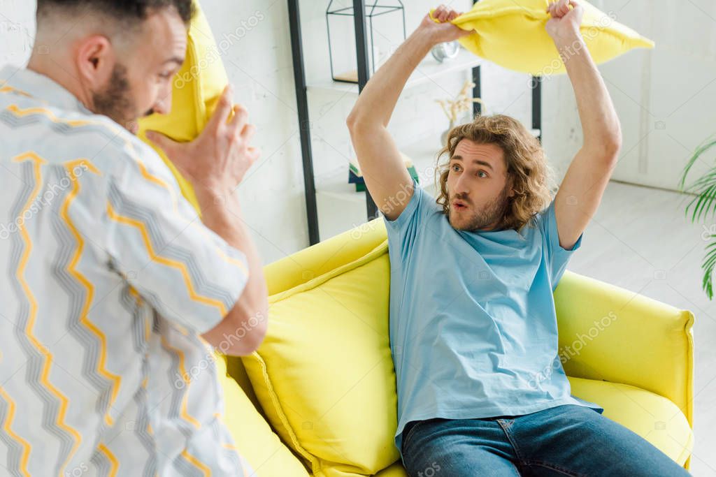 Selective focus of happy homosexual men pillow fighting in living room