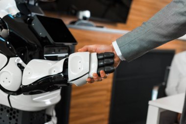 Ofisteki insansı robotla el sıkışan işadamının kısmi görüntüsü
