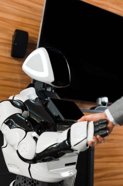 Ofisteki insansı robotla el sıkışan işadamının kısmi görüntüsü