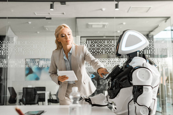 attractive businesswoman holding digital tablet while operating robot