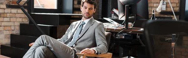 現代のオフィスのアームチェアに座っている若い自信に満ちたビジネスマンのパノラマ写真です — ストック写真