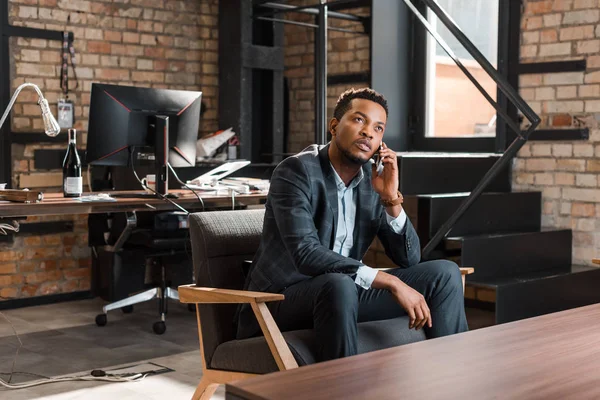 사려깊은 아프리카 미국인 사업가 의자에 앉아서 스마트폰을 하면서 올려다보고 — 스톡 사진
