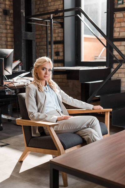 attractive, pensive businesswoman sitting in armchair and looking at camera