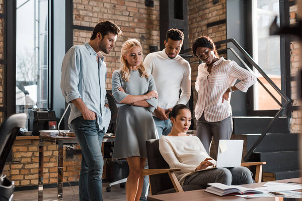 вдумчивые мультикультурные бизнесмены смотрят на азиатского коллегу, работающего над ноутбуком
 